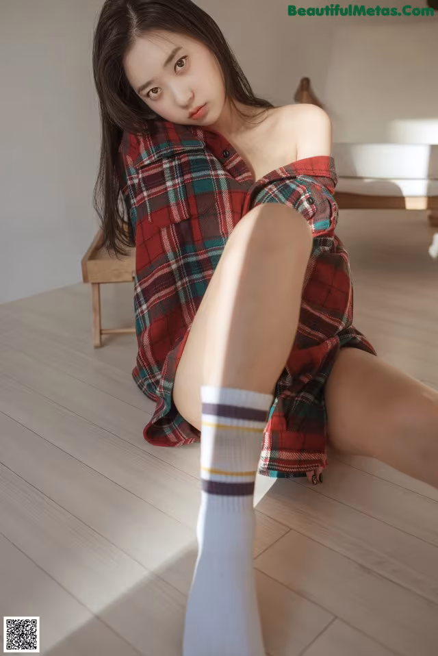 A woman in a plaid shirt and white socks sitting on the floor.
