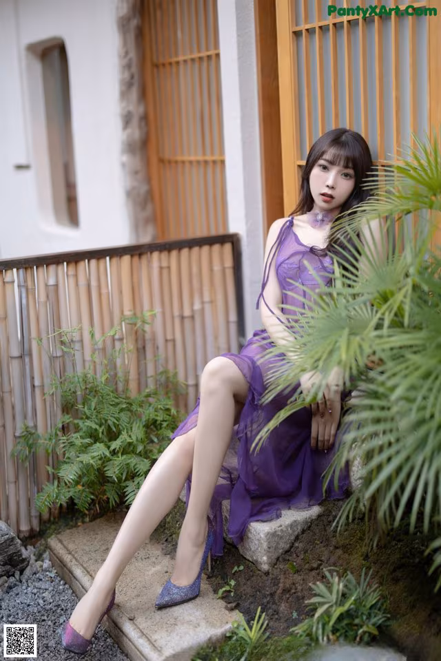 A woman in a purple dress sitting on a stone ledge.