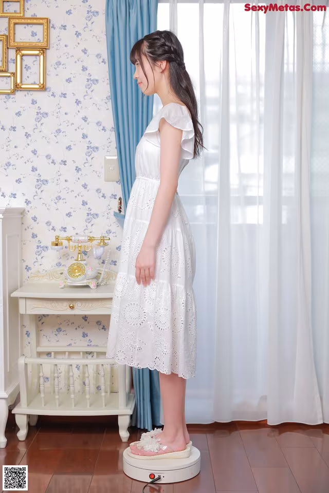 A woman in a white dress standing in front of a window.
