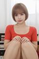 A woman in a red shirt is sitting on a bed.