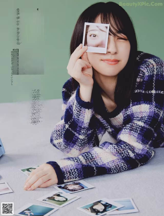 A woman sitting at a table holding a polaroid in front of her face.