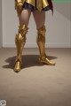 A woman in a gold outfit and boots standing in a room.