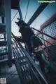 A woman in a black outfit is standing on a metal railing.