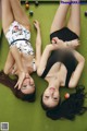 Two young women laying on a pool table with balls.