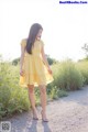 A woman in a yellow dress standing on a dirt road.