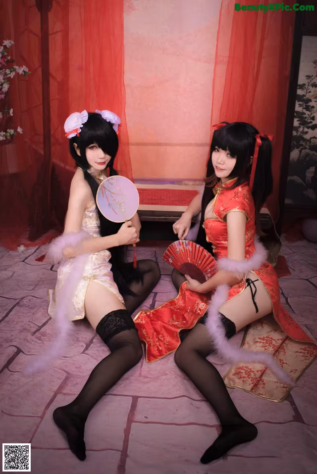 Two women dressed in chinese clothing sitting on a bed.
