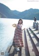 A woman in a plaid dress and straw hat standing by the water.