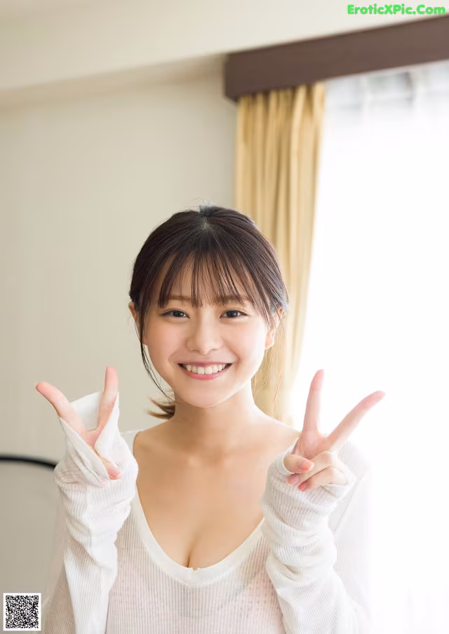 A woman in a white sweater making a peace sign with her hands.