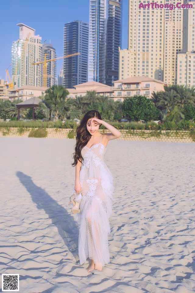 A woman in a white dress standing on a sandy beach.