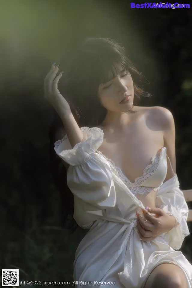 A woman in a white dress sitting on a bench.