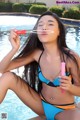 A woman in a blue bikini sitting by a swimming pool.