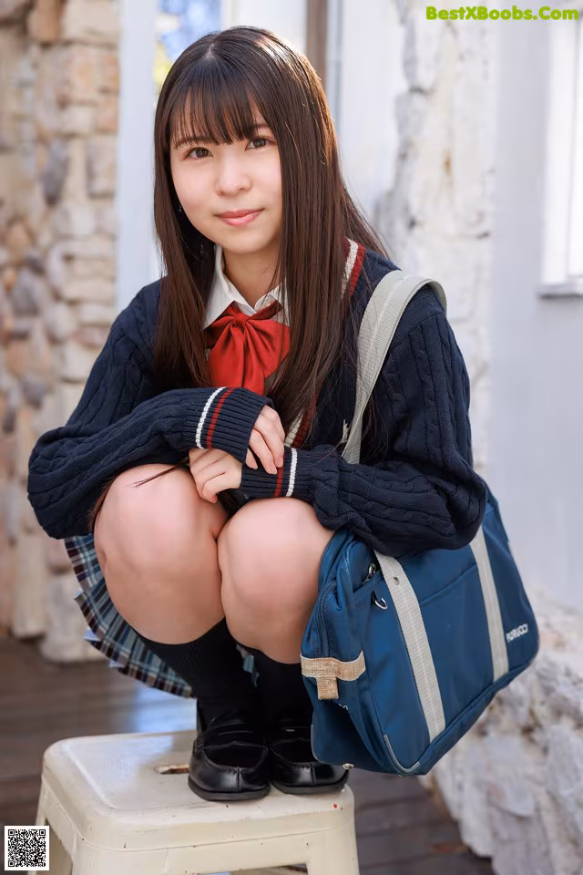 A young woman in a school uniform sitting on a stool.