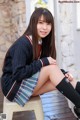 A young woman sitting on a stool wearing a school uniform.