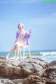 A woman sitting on a chair on a rock by the ocean.