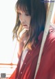 A woman in a red jacket leaning against a pole.