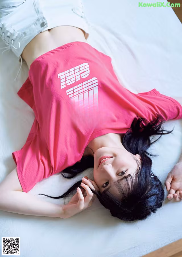 A woman laying on a bed wearing a pink shirt.