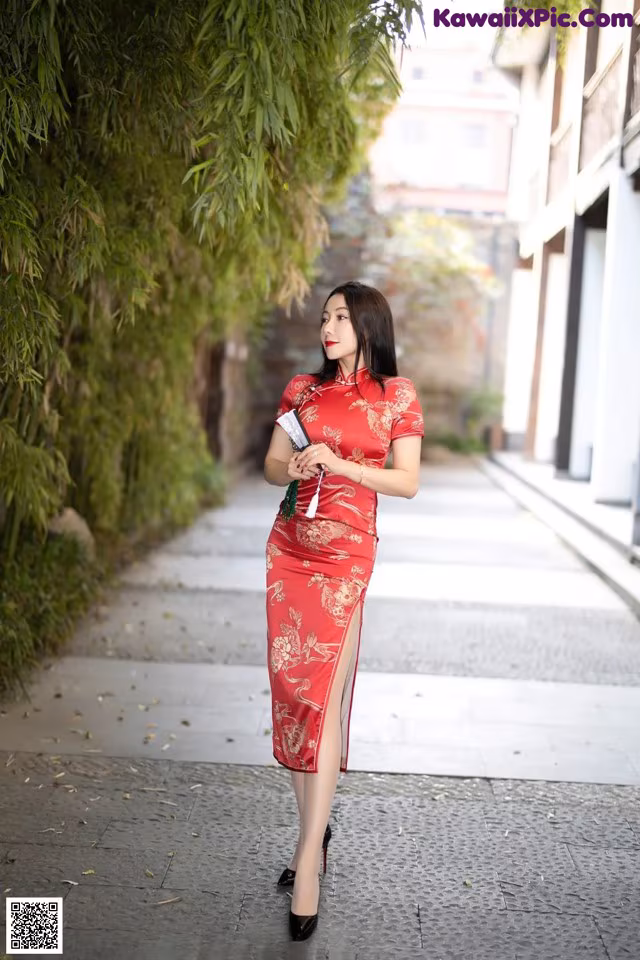A woman in a red cheongsam standing on a sidewalk.